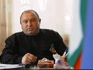 Man in Black Shirt at Desk With Pen Holder in Front of Flag