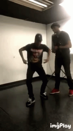 Man In Black Shirt Dancing Behind Man With Camera GIF