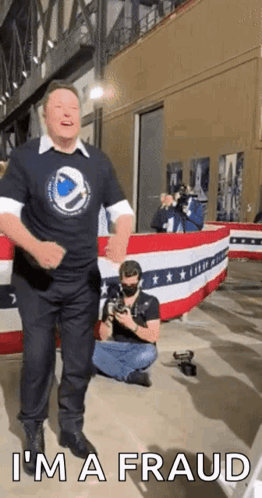 Man in Black Shirt Dancing in Front of American Flag Saying I'm a Fraud