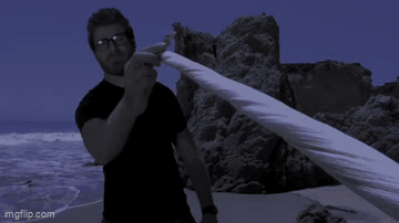 Man In Black Shirt Holding Cloth On Beach GIF