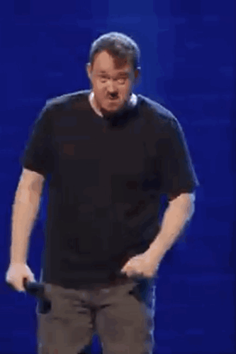 Man In Black Shirt Holding Microphone In Front Of Blue Wall GIF
