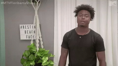 Man In Black Shirt Next To Potted Plant And Rest In Beach Face Sign GIF