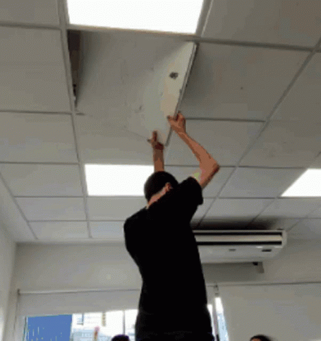 Man in Black Shirt Reaching Up to Remove Paper From Ceiling