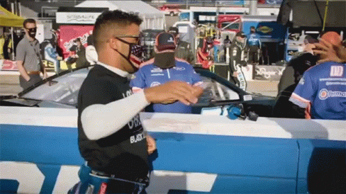Man In Black Shirt Saying Black In Front Of Race Car GIF