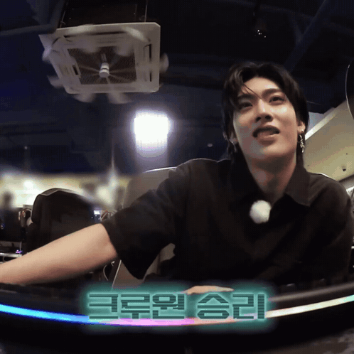 Man In Black Shirt Sitting In Front Of Korean Sign GIF