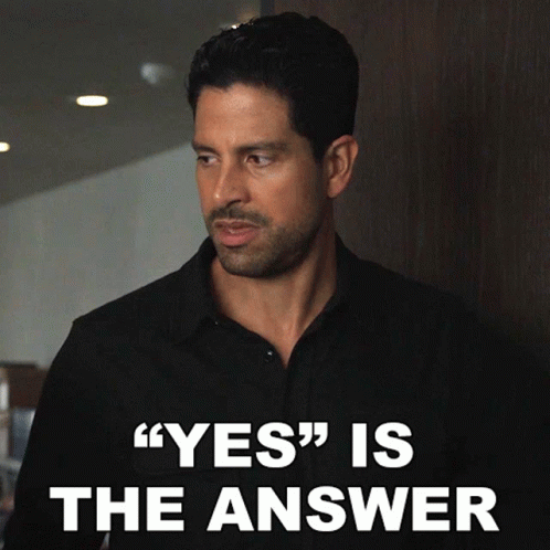 Man in Black Shirt Standing in Front of Yes Is The Answer Sign