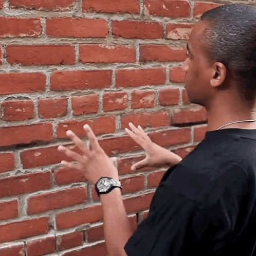 Man in Black Shirt Touching Brick Wall