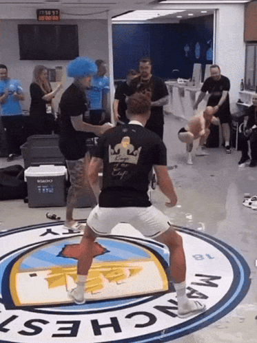 Man In Black Shirt With Crown Dancing In Front Of Manchester Logo GIF