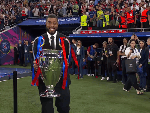 Man in Black Suit Holding Trophy in Front of Crowd