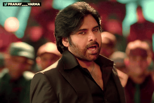 Man in Black Suit in Front of Crowd With Pranay Varma Above