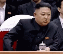 Man In Black Suit Sitting Before Group Of Men GIF