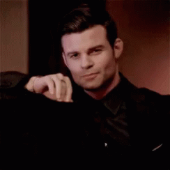 Man In Black Suit Sitting With Hand On Shoulder GIF