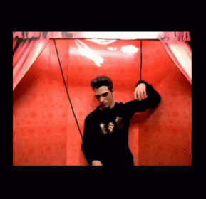 Man In Black Sweater In Front Of Red Wall GIF