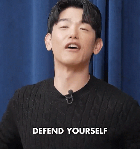 Man In Black Sweater With Microphone Says Defend Yourself GIF