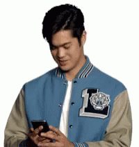 Man in Blue and Tan Varsity Jacket Looking at Cell Phone
