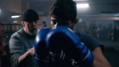 Man in Blue Boxing Gloves Being Instructed in Gym