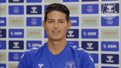 Man in Blue Everton Shirt Smiling in Front of Everton Logos