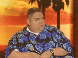 Man in Blue Floral Shirt Holding Microphone in Front of Palm Tree