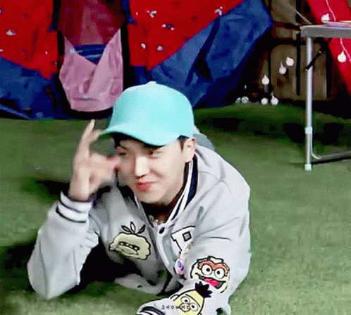 Man in Blue Hat and Gray Jacket Laying on Grass Making Funny Face