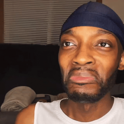 Man In Blue Hat And White Tank Top Looking At Camera GIF