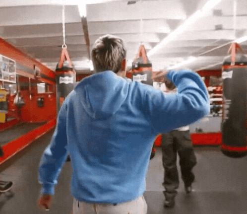 Man in Blue Hoodie in Gym With Everlast Punching Bags