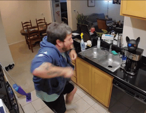 Man in Blue Hoodie in Kitchen by Sink and Coffee Maker