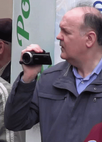 Man In Blue Jacket Holding Camera Near Po Sign GIF