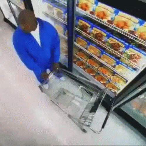 Man in Blue Jacket Pushing Shopping Cart in Front of Refrigerator