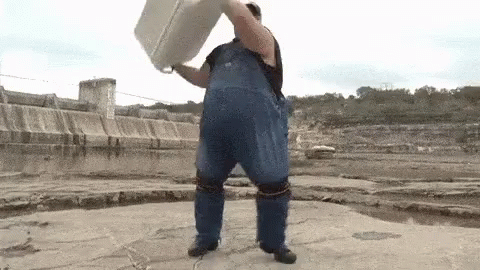 Man in Blue Overalls Holding White Bucket Over Head by Water