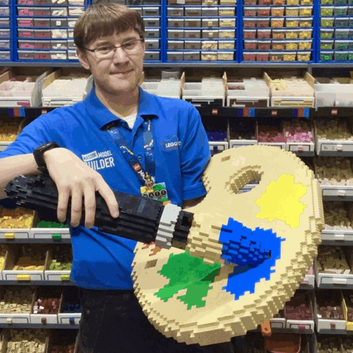 Man in Blue Power Model Builder Shirt Holding Lego Palette