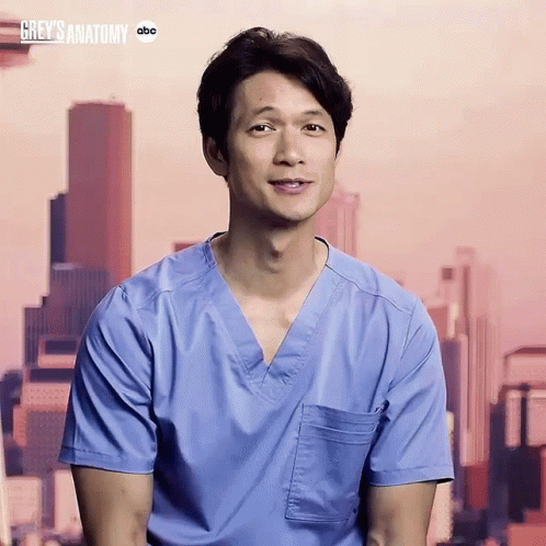 Man in Blue Scrub Smiling in Front of Grey's Anatomy Sign