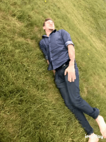 Man In Blue Shirt And Tie Laying On Grassy Hill GIF