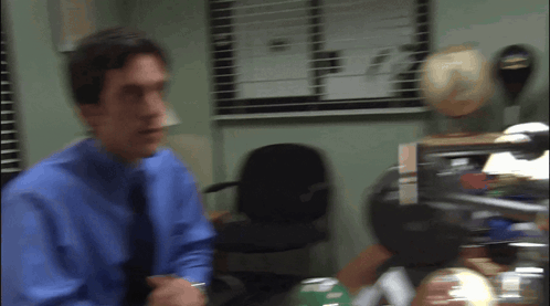 Man In Blue Shirt And Tie Standing By Window GIF