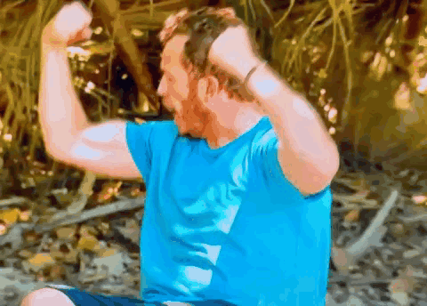 Man in Blue Shirt Flexing Muscles Sitting on Ground