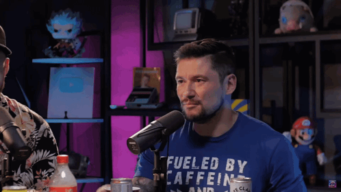 Man in Blue Shirt Fueled by Caffeine Talks Into Microphone