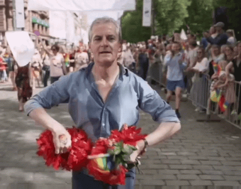 Man in Blue Shirt Holding Red Flowers in Crowd