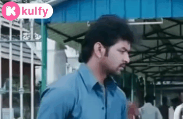 Man In Blue Shirt In Front Of Building With Kulfy Sign GIF