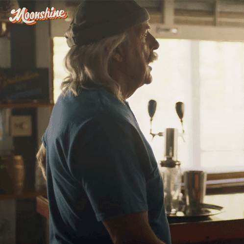 Man in Blue Shirt in Front of Moonshine Sign