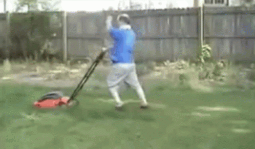 Man In Blue Shirt Mowing Lawn With Red Lawn Mower GIF