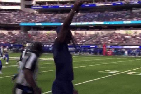 Man In Blue Shirt On Football Field With Arm Up GIF