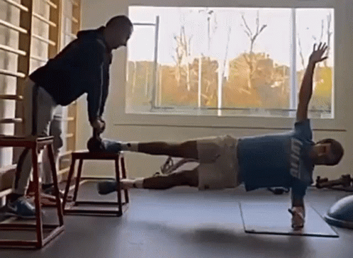 Man in Blue Shirt Planking, Another Holding Dumbbell
