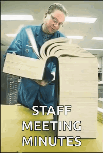 Man in Blue Shirt Reading Large Book Saying Staff Meeting Minutes