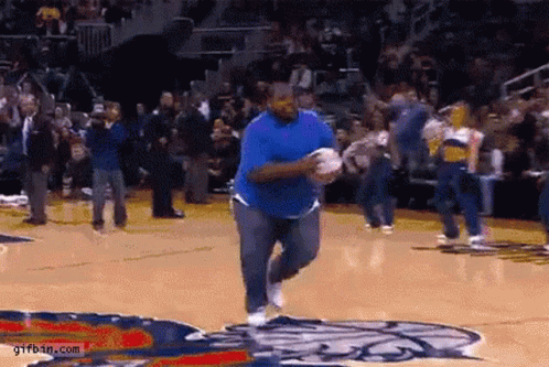 Man in Blue Shirt Running on Basketball Court in Front of Crowd