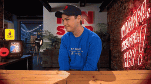 Man in Blue Shirt Sitting at Neon Hey Sign