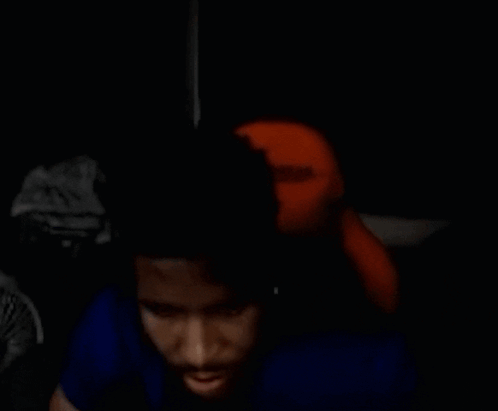 Man in Blue Shirt Sitting in Dark Room With Stuffed Animal