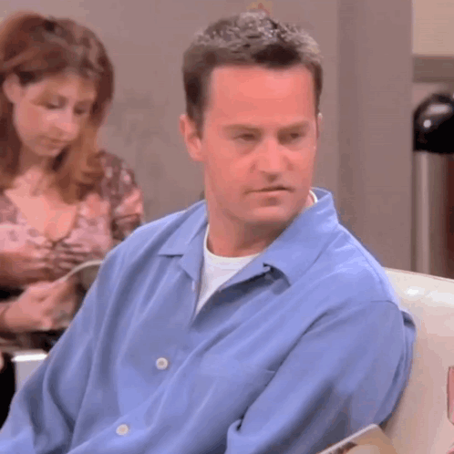 Man in Blue Shirt Sitting in Waiting Room With Woman Reading Book