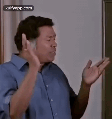 Man In Blue Shirt Standing In Front Of Blackboard Making Funny Face GIF