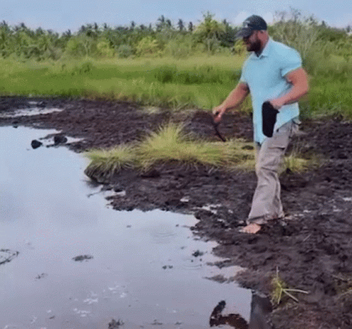 Man in Blue Shirt Standing in Muddy Field Near River