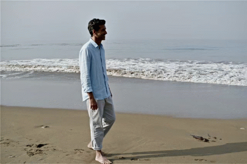 Man In Blue Shirt Walking Barefoot On Beach GIF