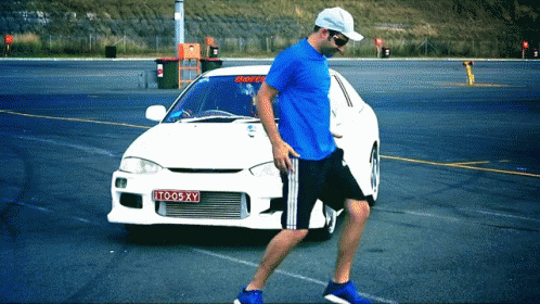 Man in Blue Shirt Walking Past White Car License Plate TO05XY